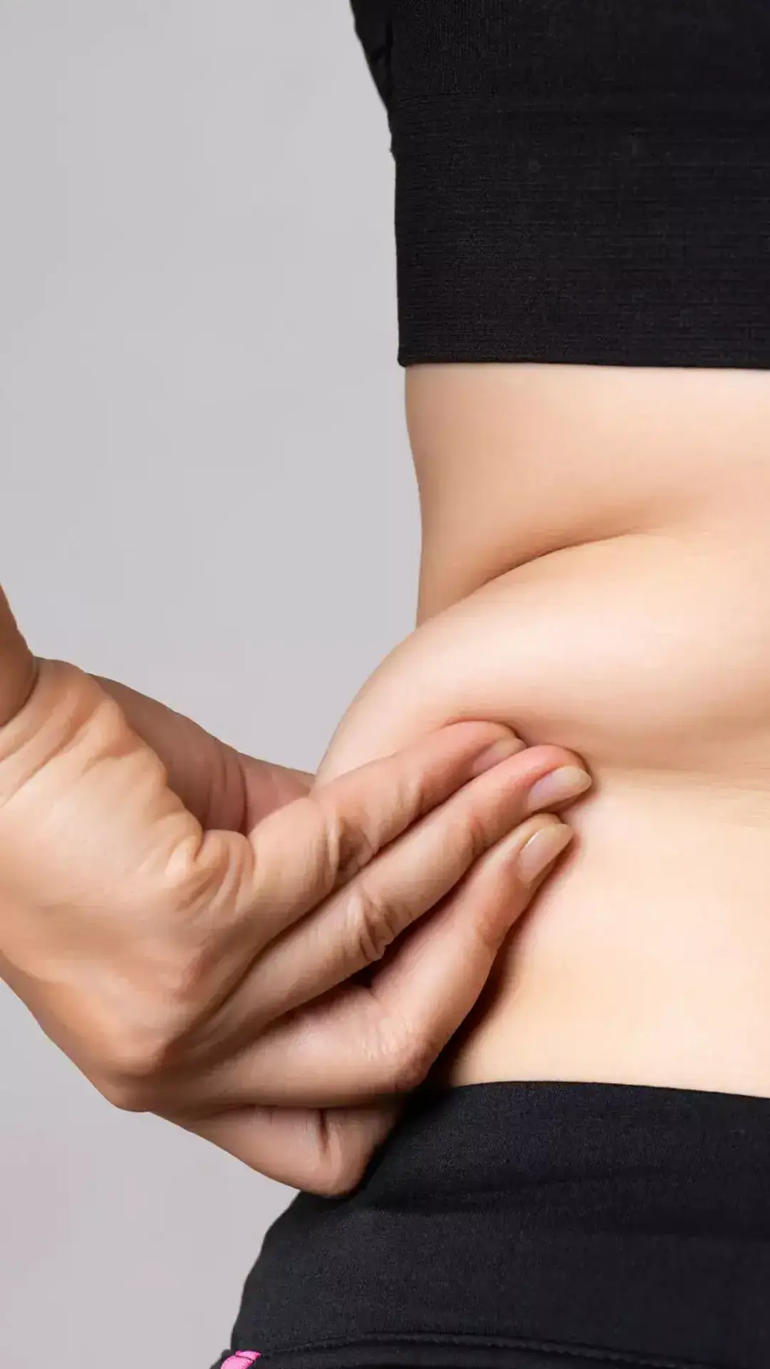 Hand pinching belly fat on waist area before fat reduction or body contouring