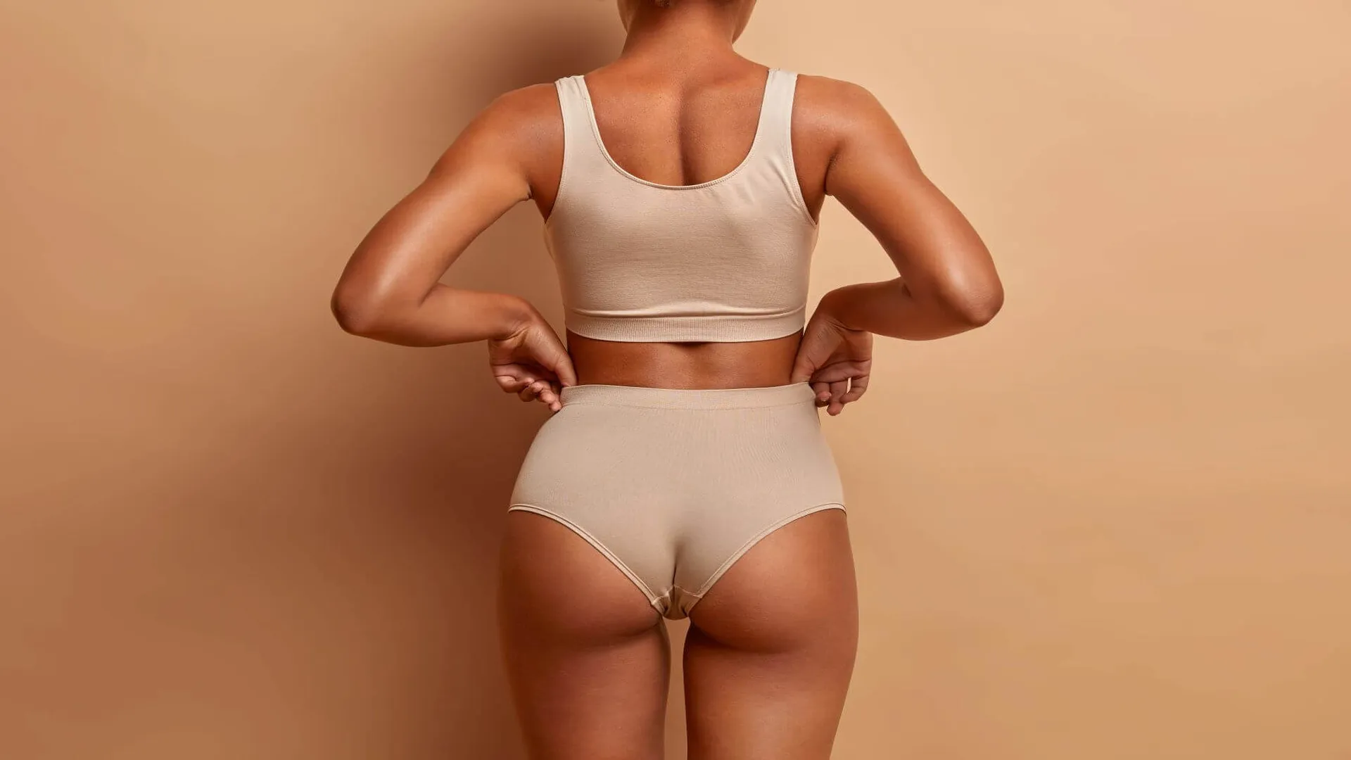 Fit woman in beige shapewear showing toned back and enhanced curves on neutral background