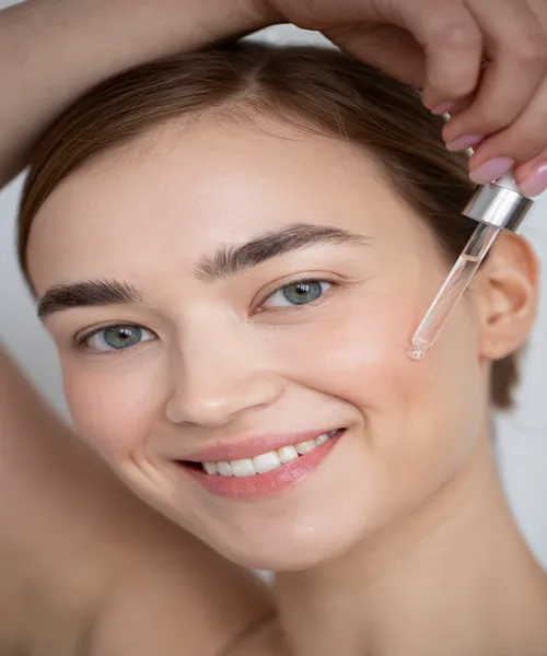 Smiling woman applying facial serum with dropper for glowing skin care routine